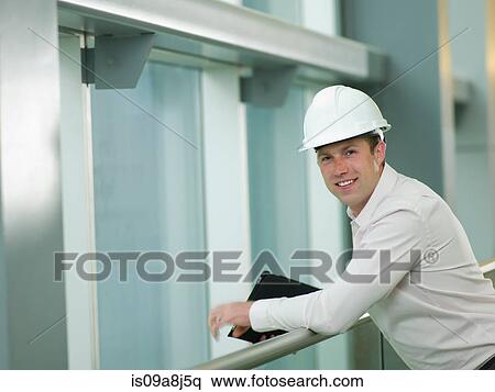 Stock Photography - Mid adult construction worker in hard hat leaning on railing, portrait. Fotosearch