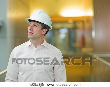 Stock Photography - Mid adult construction worker in hard hat, looking up. Fotosearch