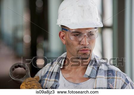 Stock Image - Mid adult construction worker wearing hard hat, looking away. Fotosearch