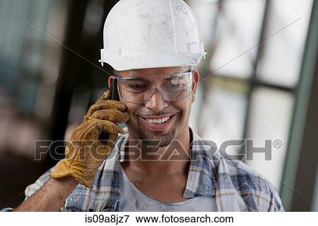 Stock Photo - Mid adult construction worker wearing hard hat and using mobile phone. Fotosearch