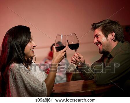 Stock Image - Mid adult couple toasting with wine in restaurant, smiling. Fotosearch