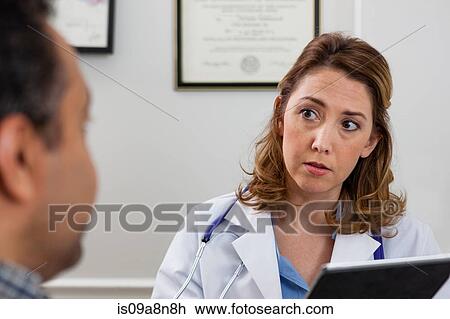 Stock Image - Mid adult doctor using digital tablet and listening to patient. Fotosearch