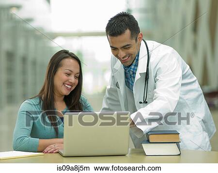 Mid adult doctor using laptop with young student, smiling View Large Photo Image Picture - Mid adult doctor using laptop with young student, smiling. Fotosearch