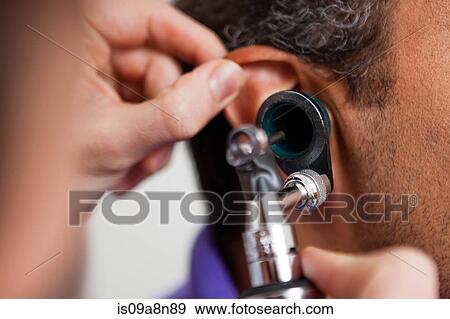 Stock Photo - Mid adult doctor using otoscope on patient. Fotosearch
