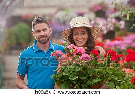 Stock Image - Mid adult man and young woman holding plants in garden centre, portrait. Fotosearch