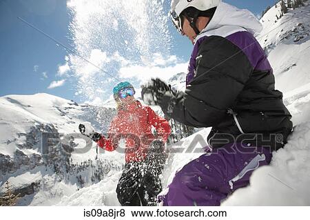Stock Photo - Mid adult man and young woman in skiwear having snowball fight. Fotosearch