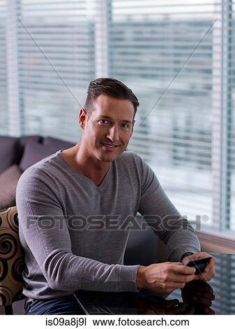 Mid adult man sitting and holding mobile phone View Large Photo Image Stock Image - Mid adult man sitting and holding mobile phone. Fotosearch