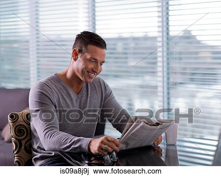 Stock Image - Mid adult man sitting and reading newspaper. Fotosearch