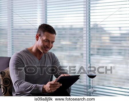 Stock Image - Mid adult man sitting and using digital tablet. Fotosearch