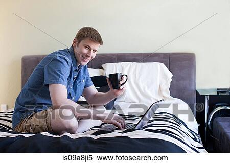Stock Photography - Mid adult man sitting on bed using laptop, portrait. Fotosearch