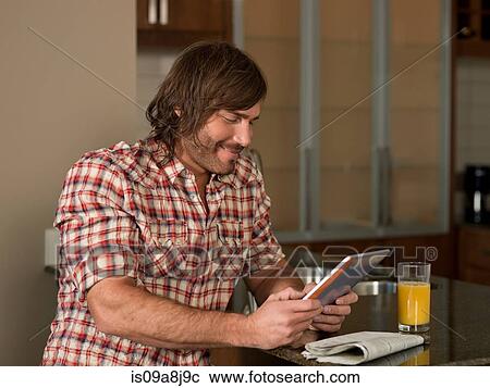 Stock Image - Mid adult man using digital tablet in kitchen. Fotosearch