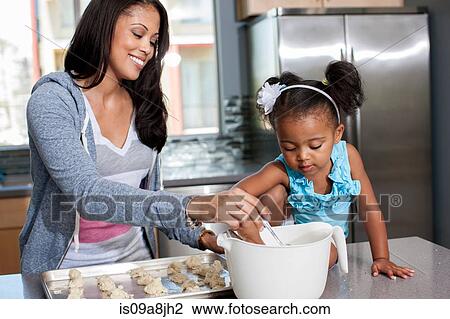 Stock Image - Mid adult woman baking with daughter in kitchen. Fotosearch