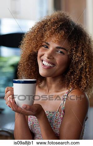 Stock Image - Mid adult woman enjoying coffee in kitchen, portrait. Fotosearch