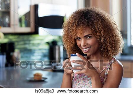 Stock Photo - Mid adult woman enjoying coffee in kitchen, portrait. Fotosearch