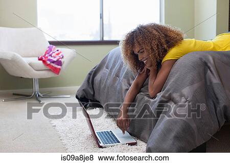 Stock Photo - Mid adult woman lying on bed using laptop. Fotosearch