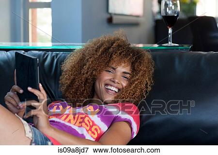 Mid adult woman sitting holding electronic book on sofa, smiling View Large Photo Image Stock Photo - Mid adult woman sitting holding electronic book on sofa, smiling. Fotosearch