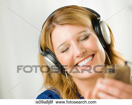 Mid adult woman wearing headphones and listening to mp3 player View Large Photo Image Stock Image - Mid adult woman wearing headphones and listening to mp3 player. Fotosearch