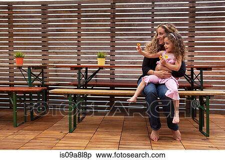 Stock Photography - Mother and daughter sitting on bench on patio. Fotosearch