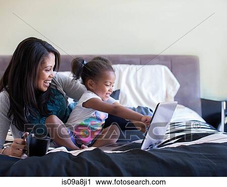 Stock Image - Mother and daughter using laptop on bed. Fotosearch