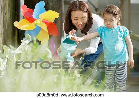 Stock Image - Mother and daughter with watering can and toy windmill. Fotosearch