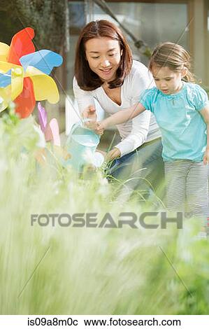 Stock Image - Mother and young daughter with watering can and toy windmill. Fotosearch