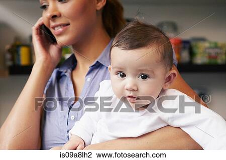 Stock Image - Mother holding baby girl whilst on the phone. Fotosearch