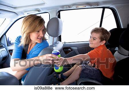Stock Image - Mother passing bottle to boy in back seat of car. Fotosearch