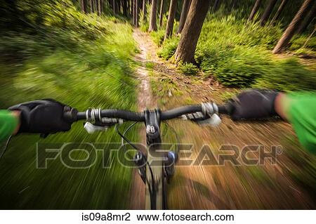 Stock Image - Mountain biker speeding down forest path. Fotosearch