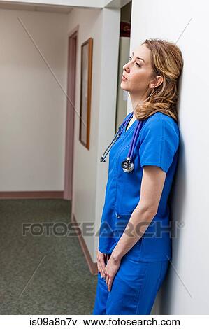 Nurse in blue scrubs in leaning against wall in hospital corridor View Large Photo Image Stock Photo - Nurse in blue scrubs in leaning against wall in hospital corridor. Fotosearch