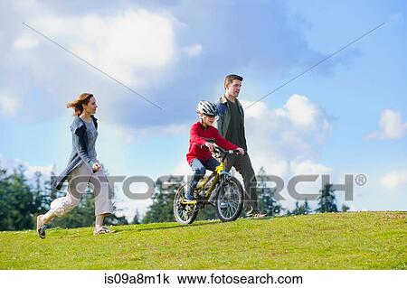 Stock Image - Parents keeping up with son riding bicycle. Fotosearch