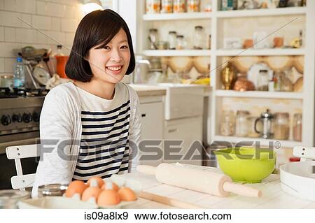 Stock Photo - Portrait of young woman at kitchen table with baking ingredients. Fotosearch