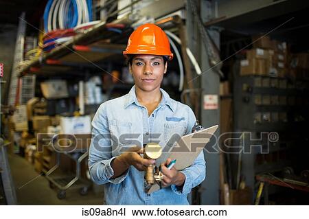 Stock Image - Portrait of young woman in warehouse with clipboard. Fotosearch