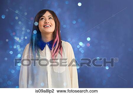 Stock Image - Portrait of young woman looking up at glitter. Fotosearch