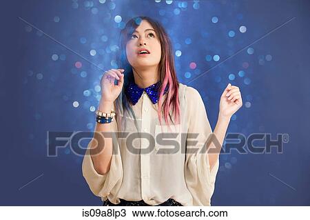 Stock Image - Portrait of young woman looking up at glitter. Fotosearch