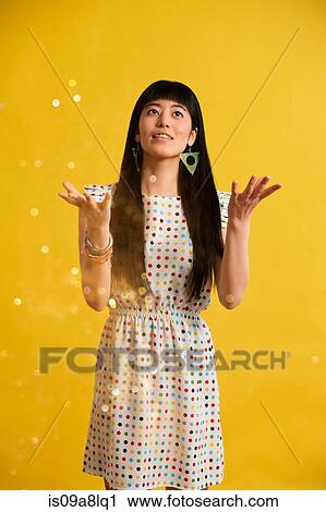 Stock Image - Portrait of young woman wearing spotted dress catching glitter. Fotosearch