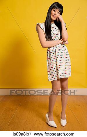 Stock Photo - Portrait of young woman wearing spotted dress with hand on chin. Fotosearch