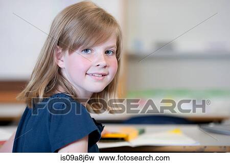 Stock Photo - Schoolgirl sitting at desk in school and smiling, portrait. Fotosearch
