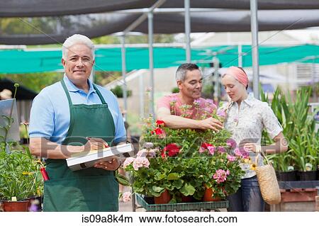 Senior gardener using clipboard with customers in background of garden centre View Large Photo Image Picture - Senior gardener using clipboard with customers in background of garden centre. Fotosearch