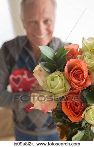 Stock Image - Senior man holding bunch of flowers and chocolates. Fotosearch