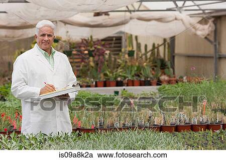 Stock Image - Senior man holding clipboard in garden centre, portrait. Fotosearch