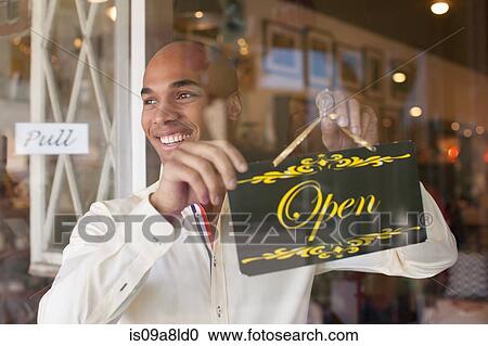 Stock Image - Shopkeeper turning open sign on vintage shop door. Fotosearch