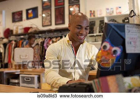 Stock Image - Shopkeeper using computer in vintage shop. Fotosearch