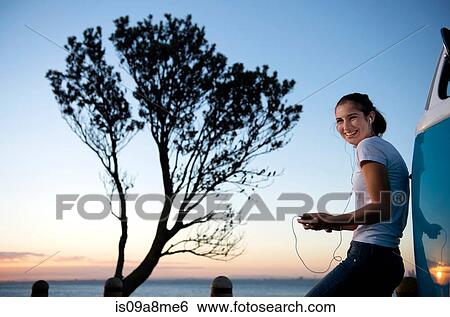 Smiling young woman leaning on camper van at dusk View Large Photo Image Stock Photograph - Smiling young woman leaning on camper van at dusk. Fotosearch
