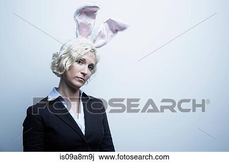Stock Image - Studio portrait of blond businesswoman wearing bunny ears. Fotosearch