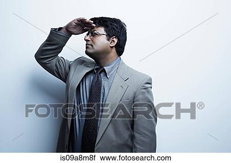 Stock Image - Studio portrait of businessman with hand shading eyes. Fotosearch