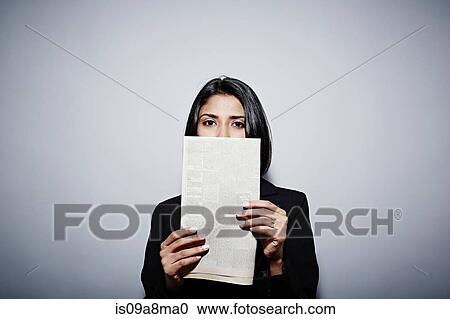 Stock Image - Studio portrait of businesswoman holding up newspaper. Fotosearch