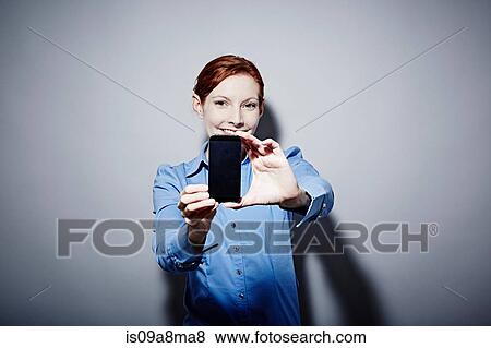 Stock Photo - Studio portrait of young woman holding up camera phone. Fotosearch