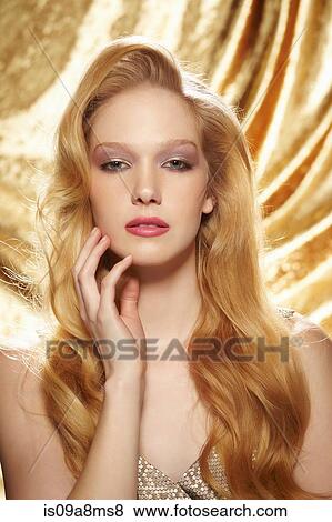 Stock Photo - Studio portrait of young woman in front of gold curtain. Fotosearch
