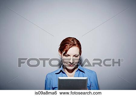 Studio portrait of young woman looking down at digital tablet View Large Photo Image Stock Photograph - Studio portrait of young woman looking down at digital tablet. Fotosearch