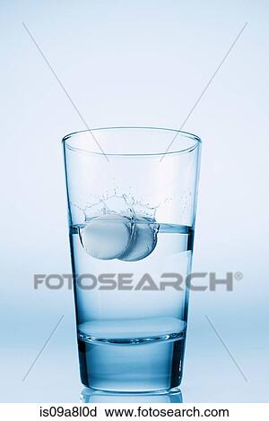 Stock Image - Tablets falling in glass of water. Fotosearch
